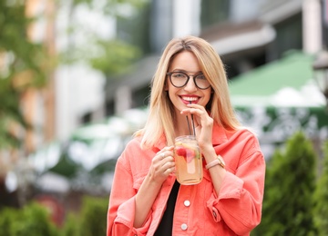 Young woman with mason jar of tasty lemonade outdoors