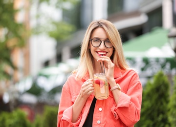 Photo of Young woman with mason jar of tasty lemonade outdoors