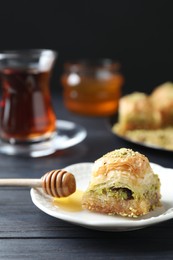Photo of Delicious fresh baklava and honey with chopped nuts on black wooden table, closeup. Eastern sweets