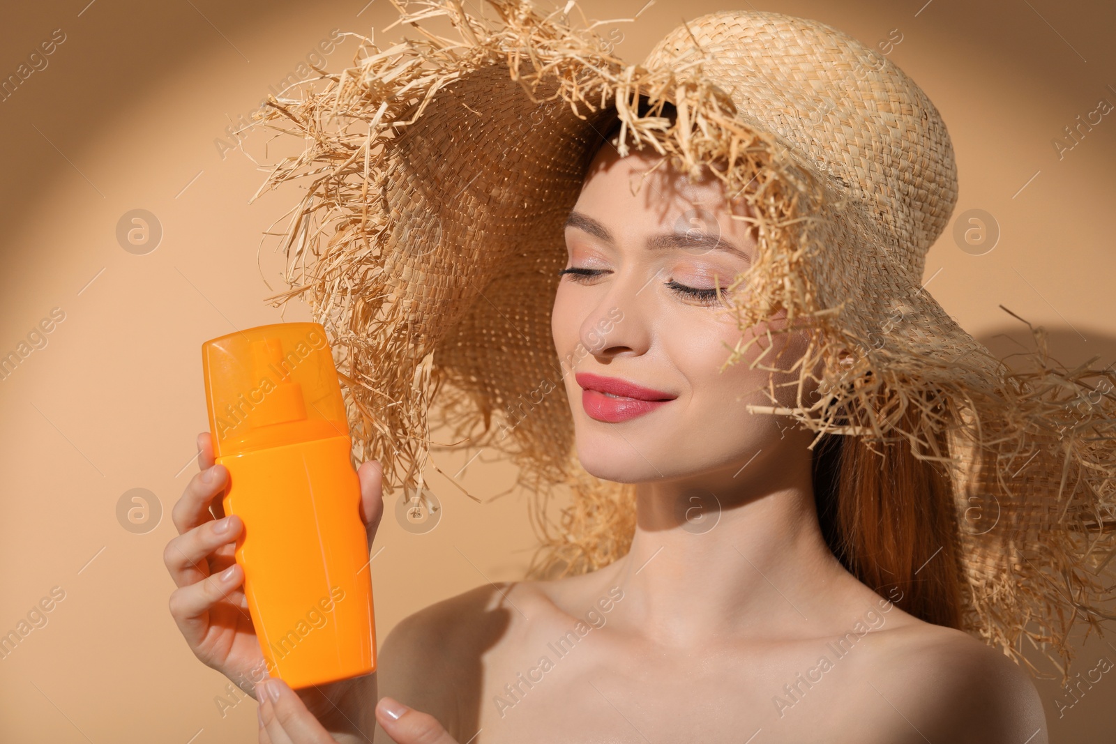Photo of Beautiful young woman in sunlight holding sun protection cream on beige background