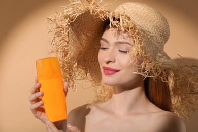 Beautiful young woman in sunlight holding sun protection cream on beige background