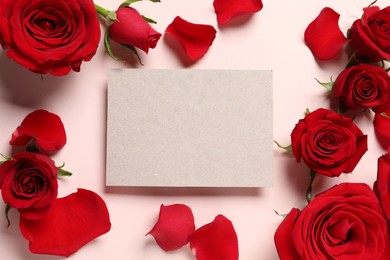 Blank card, beautiful red roses and petals on pale pink background, flat lay. Space for text