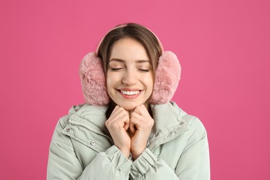 Happy woman wearing warm earmuffs on pink background