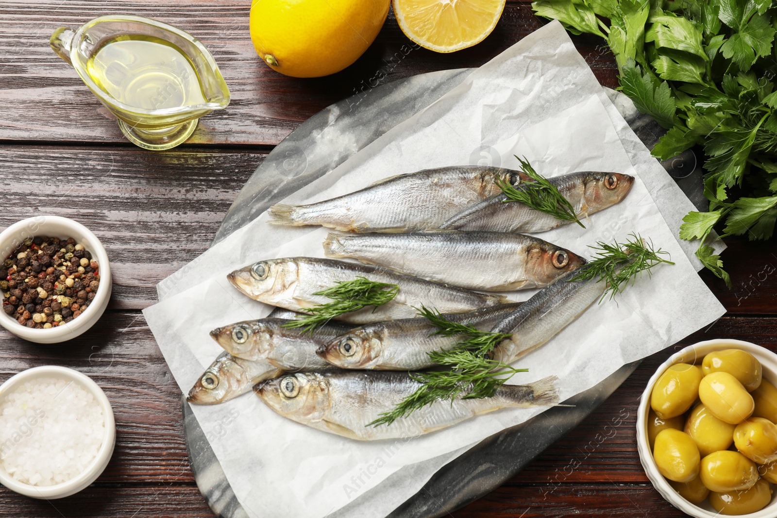 Photo of Fresh raw sprats, dill and other products on wooden table, flat lay