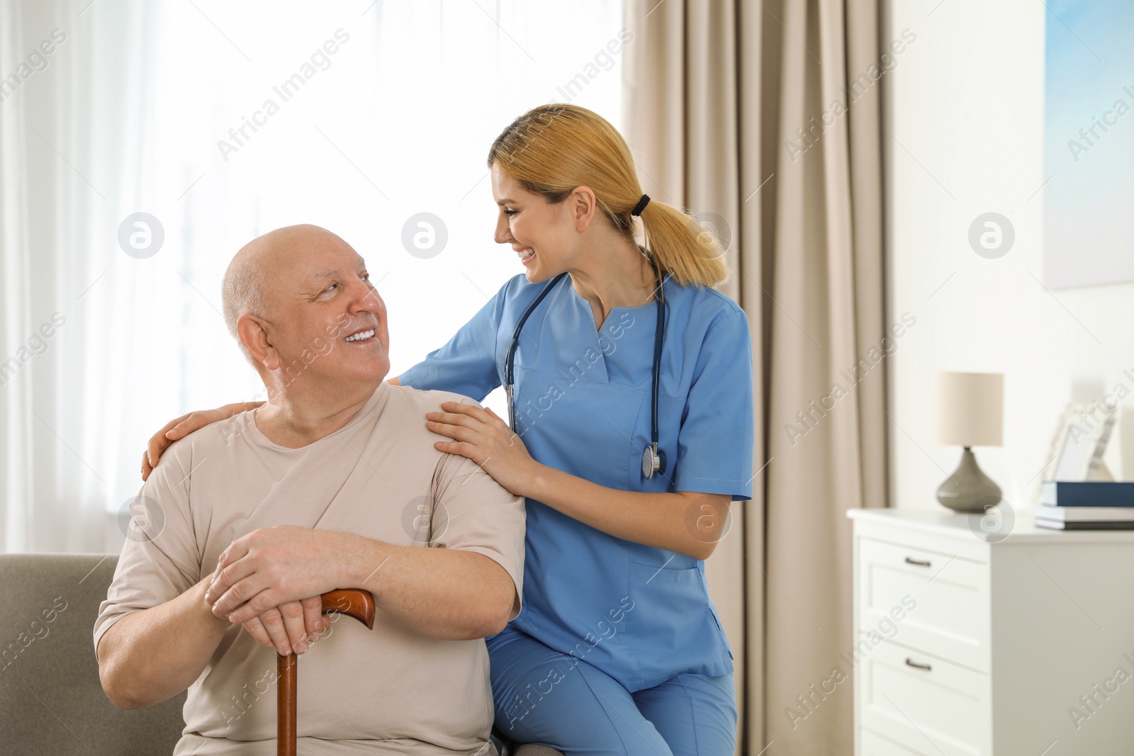 Photo of Nurse assisting elderly man with cane indoors