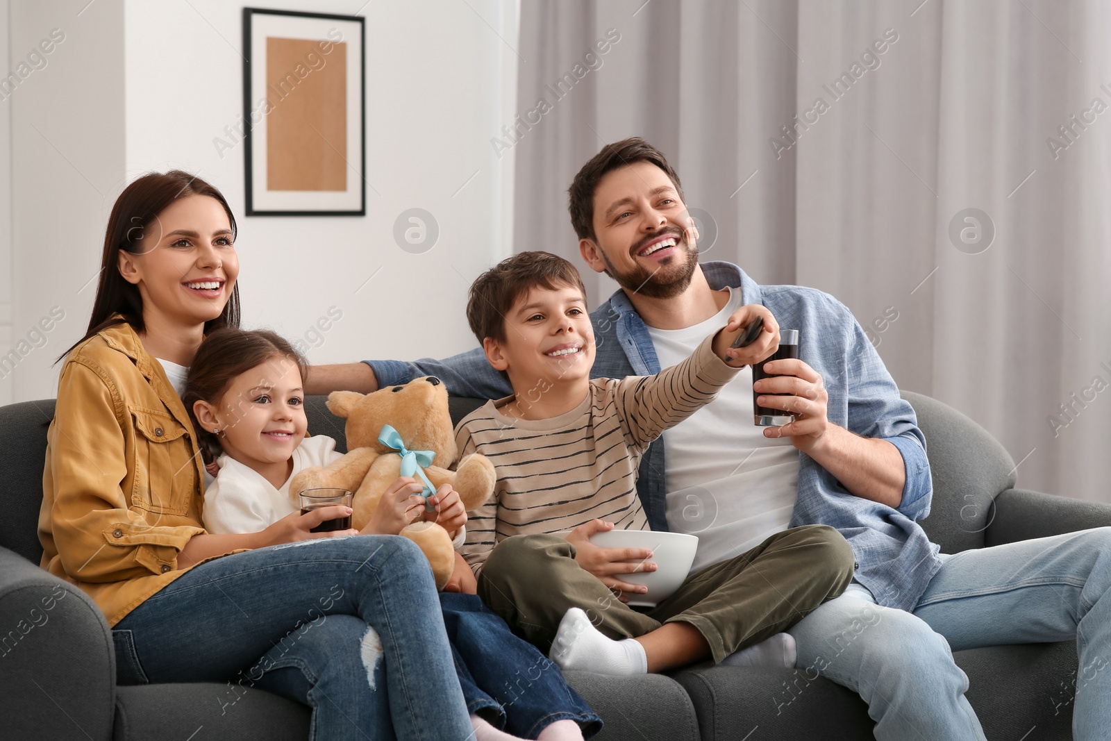 Photo of Happy family watching TV at home. Son changing channels with remote control