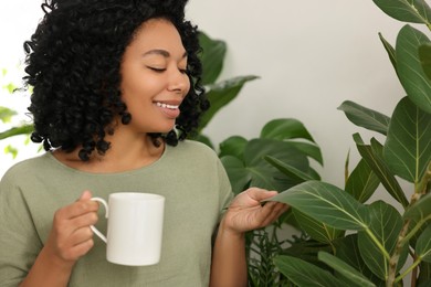 Relaxing atmosphere. Happy woman with cup of hot drink near beautiful houseplants