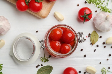 Photo of Glass jar of pickled cherry tomatoes on white wooden table, flat lay