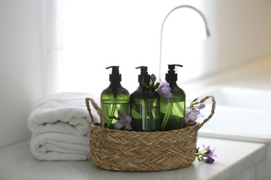 Photo of Wicker basket with soap dispensers , flowers and clean towels on table