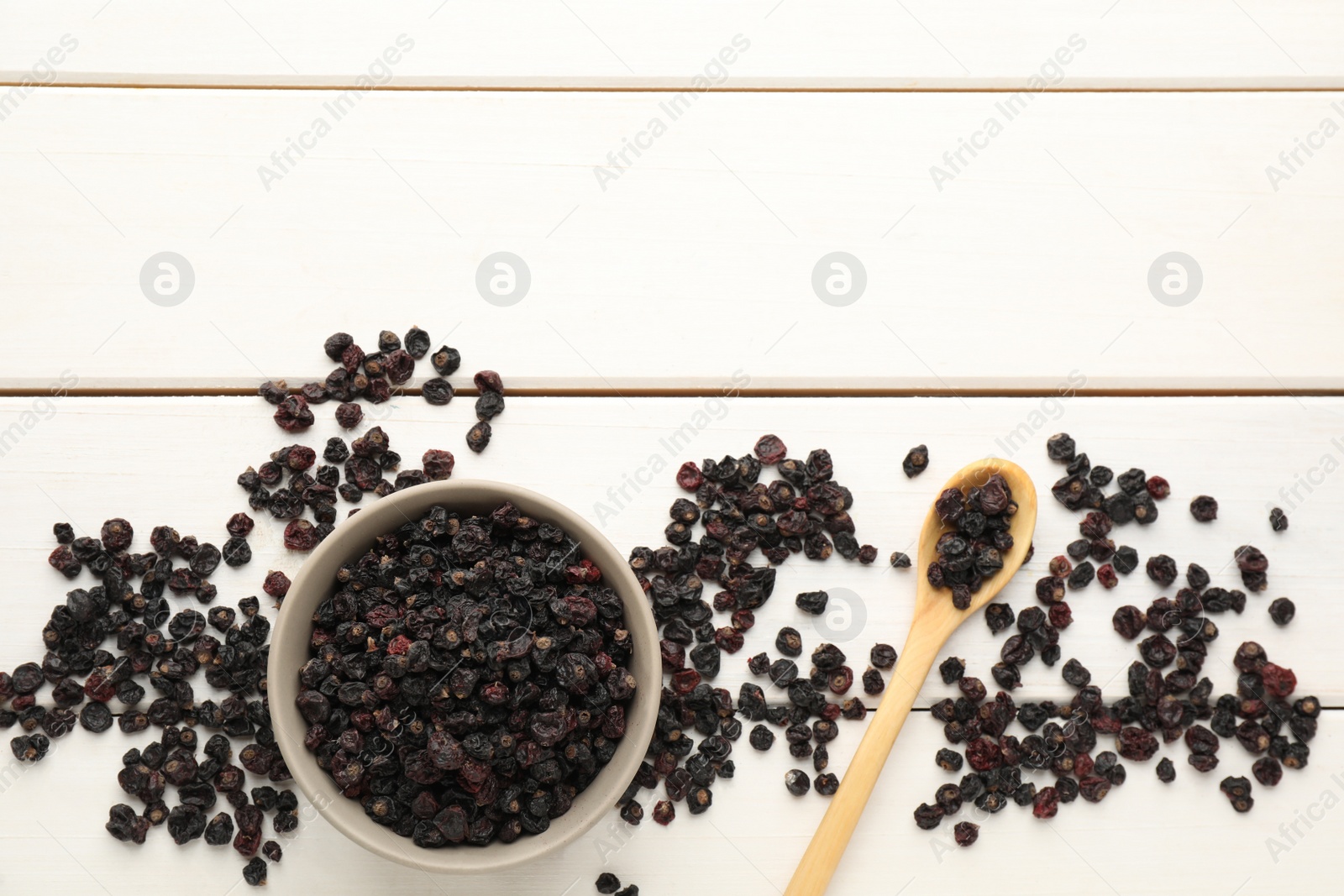 Photo of Dried black currants, bowl and spoon on white wooden table, flat lay. Space for text