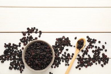 Dried black currants, bowl and spoon on white wooden table, flat lay. Space for text