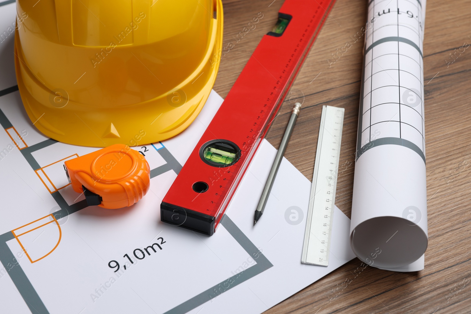 Photo of Construction drawings, safety hat, tape measure and bubble level on wooden table