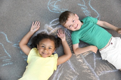 Photo of Little children lying near chalk drawing on asphalt, top view
