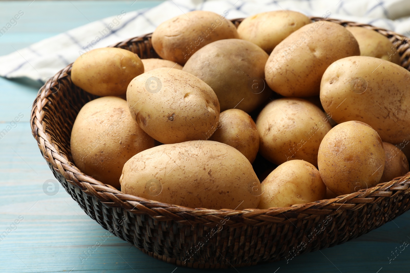 Photo of Raw fresh potatoes in wicker basket on light blue wooden table