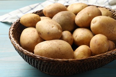 Raw fresh potatoes in wicker basket on light blue wooden table