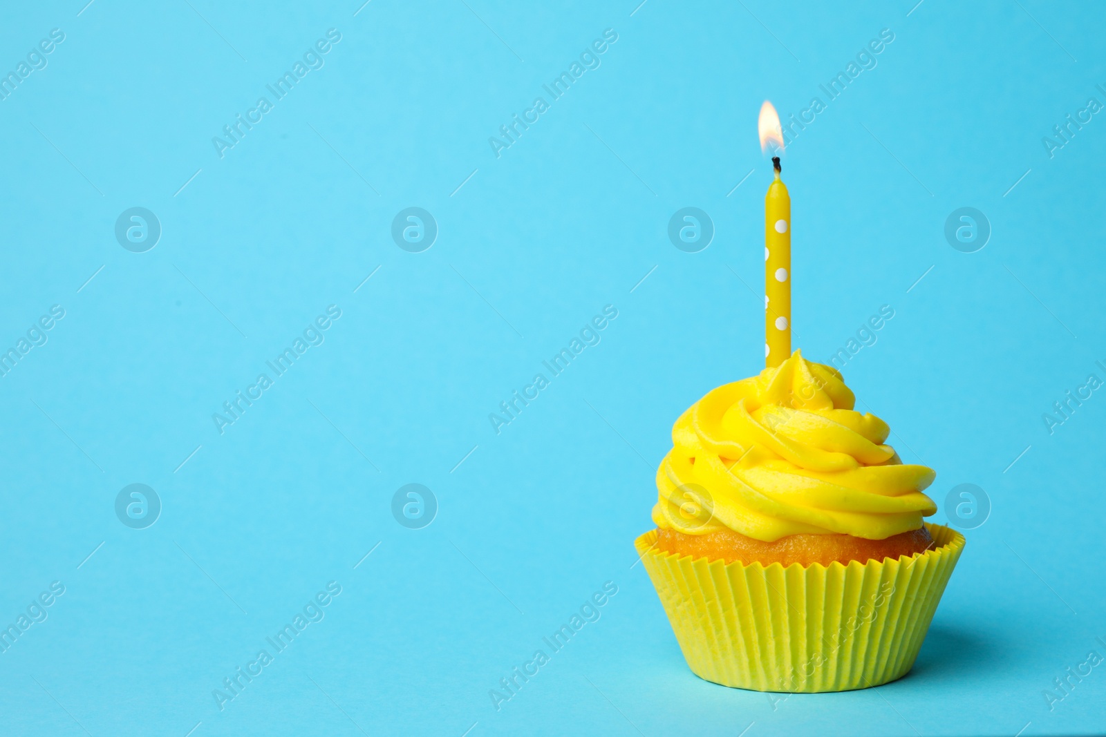 Photo of Delicious birthday cupcake with yellow cream and burning candle on light blue background. Space for text
