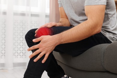 Man suffering from pain in knee indoors, closeup