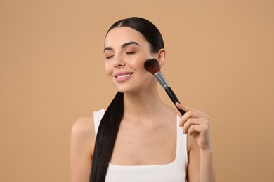 Beautiful woman applying makeup on light brown background