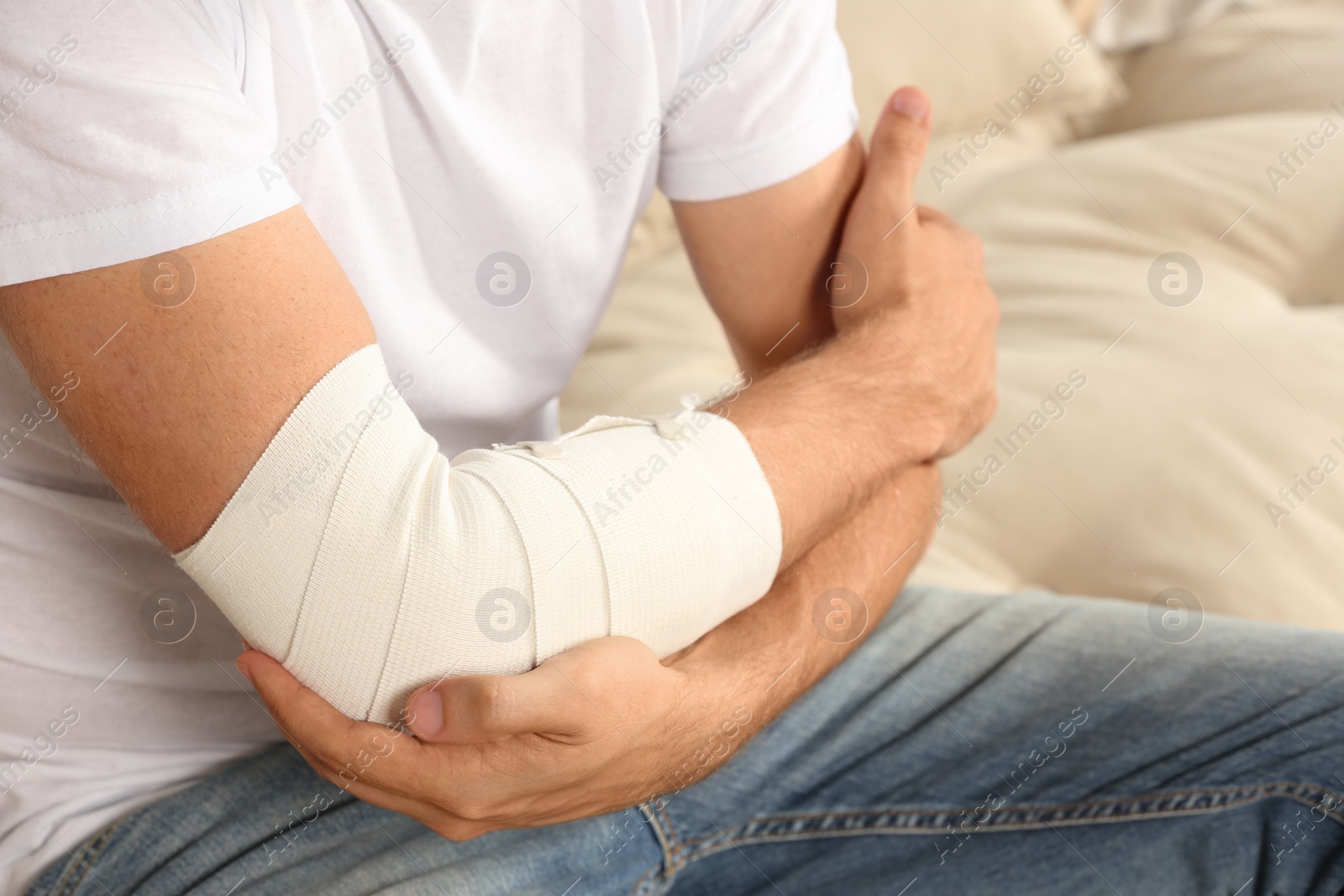 Photo of Man with arm wrapped in medical bandage on sofa, closeup