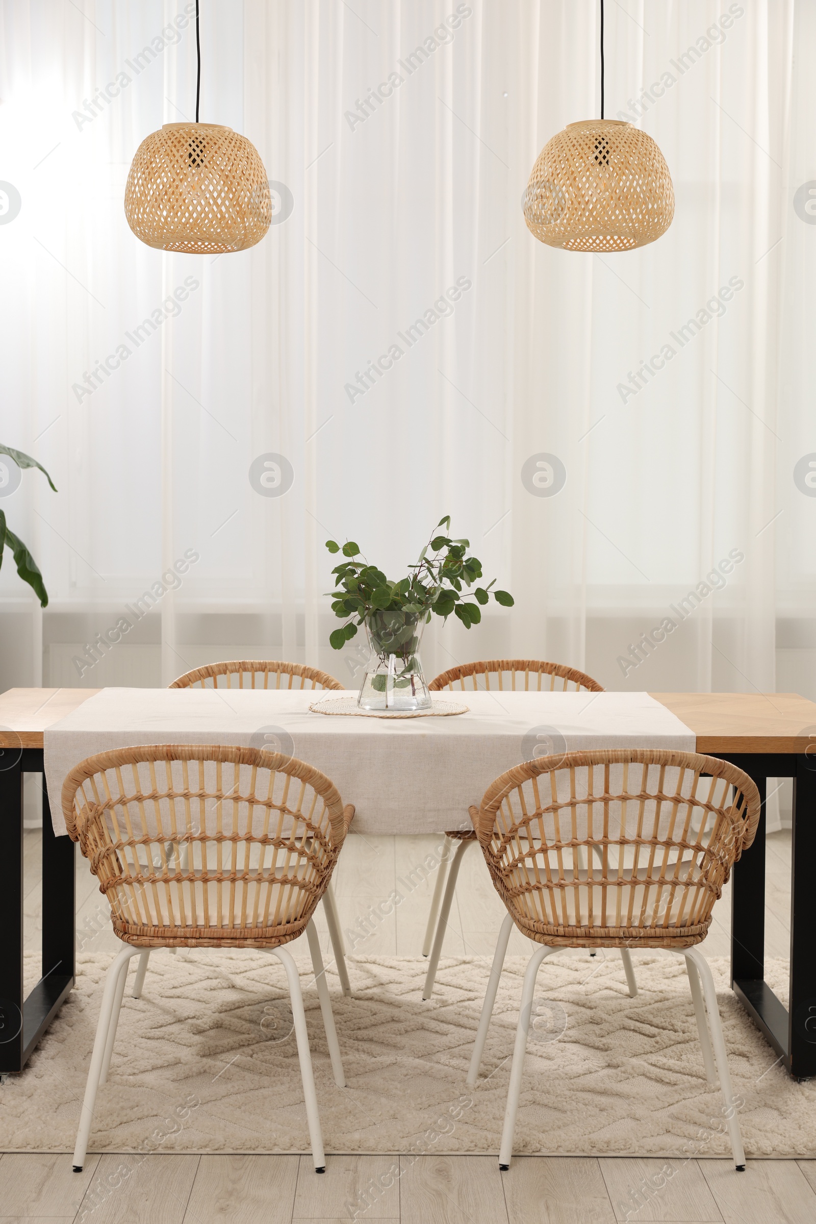Photo of Vase with eucalyptus branches on table and chairs in dining room