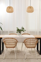 Vase with eucalyptus branches on table and chairs in dining room