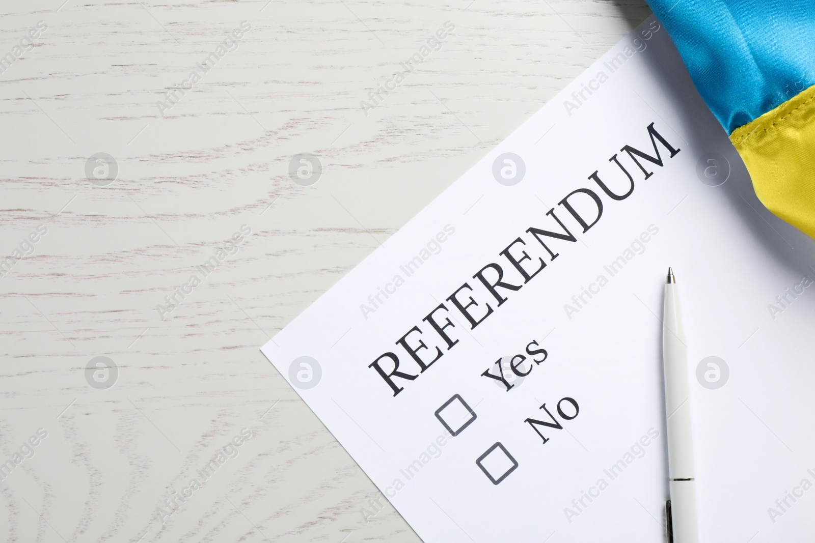 Photo of Referendum ballot with pen and flag of Ukraine on white wooden table, flat lay. Space for text