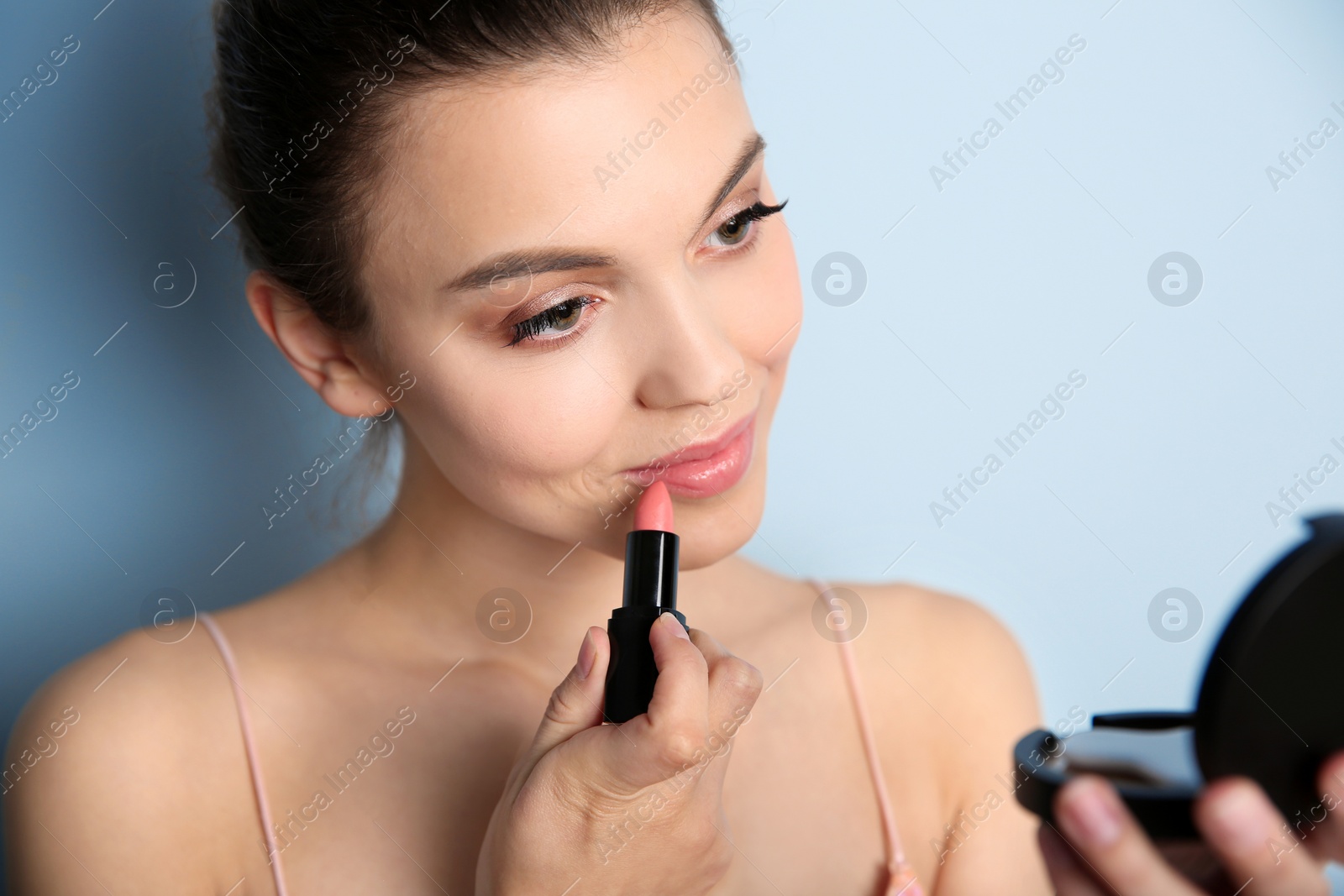 Photo of Young woman applying lipstick on color background. Professional makeup products