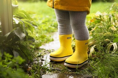 Little girl wearing rubber boots standing in puddle outdoors, closeup