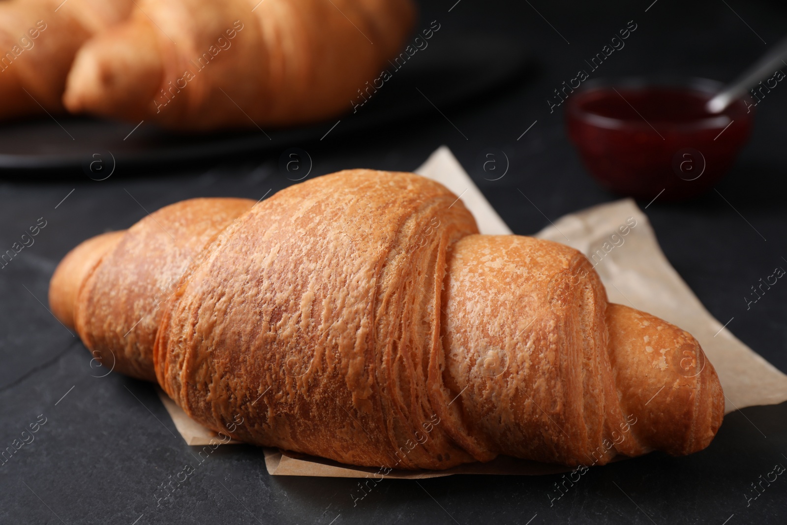 Photo of Tasty fresh croissant on black table, closeup
