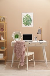 Photo of Cozy workplace with modern laptop on desk and comfortable chair at home