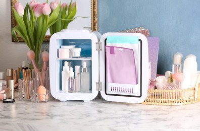 Photo of Open mini cosmetics refrigerator and skin care products on white marble table