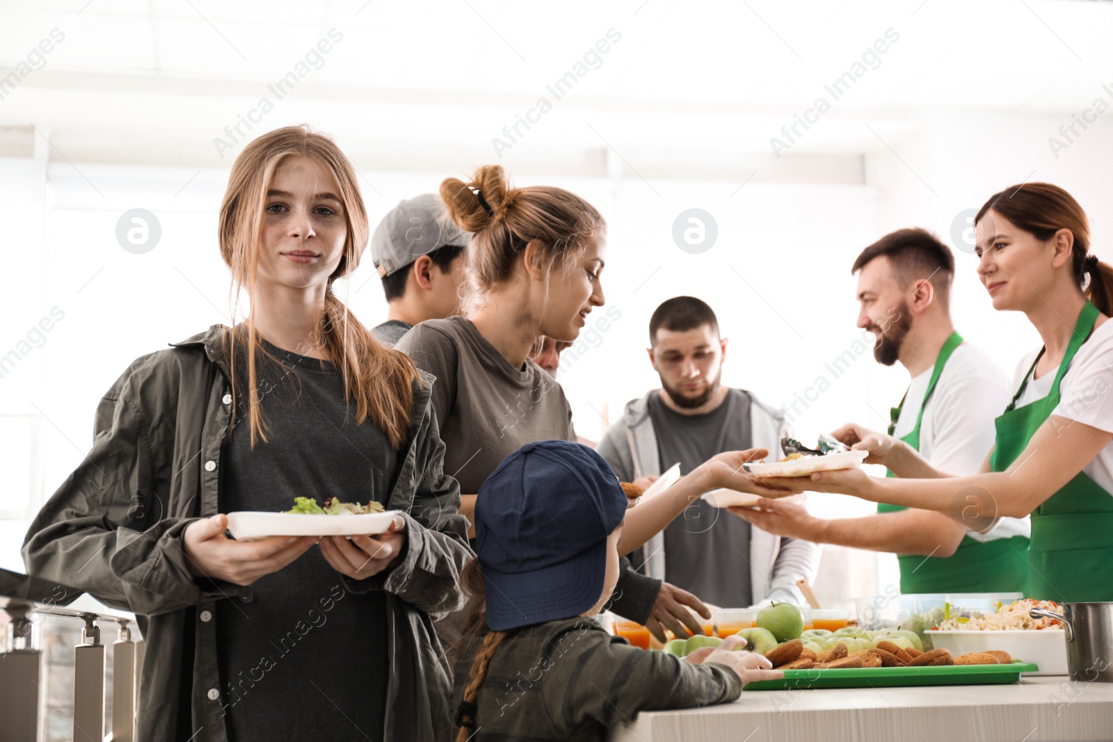 Photo of Teenage girl with other poor people receiving food from volunteers indoors