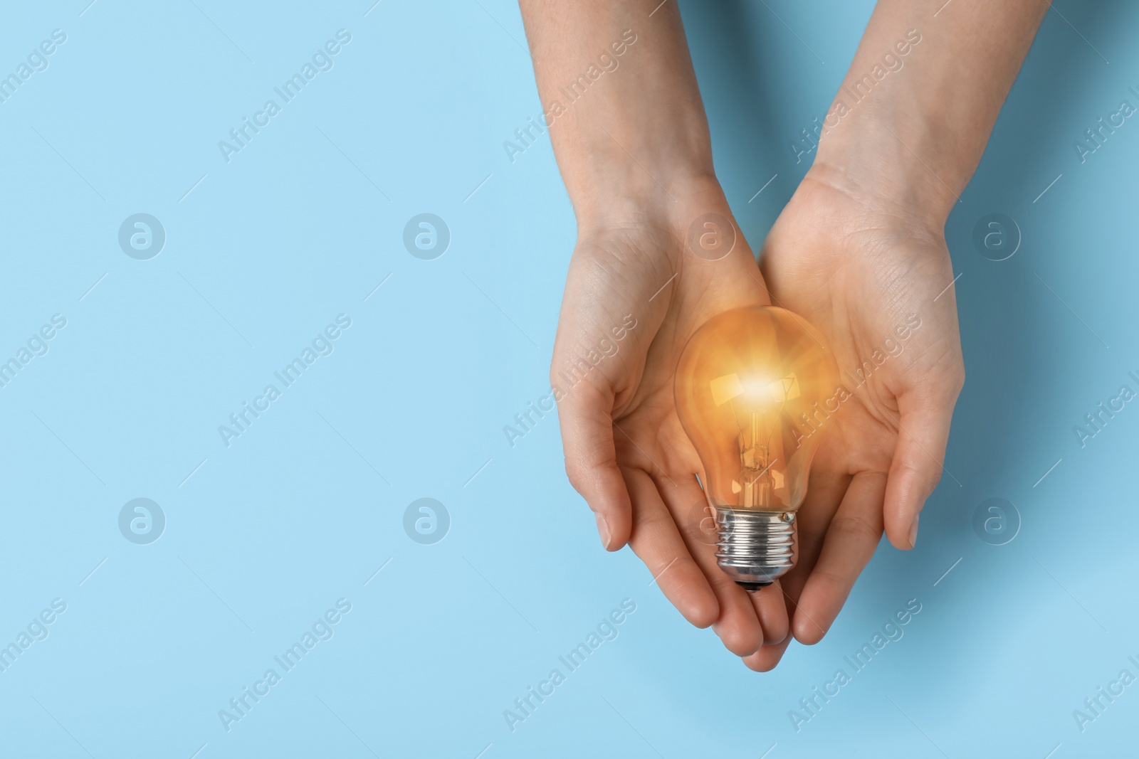 Image of Woman holding glowing light bulb on blue background, top view. Space for text