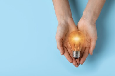 Image of Woman holding glowing light bulb on blue background, top view. Space for text