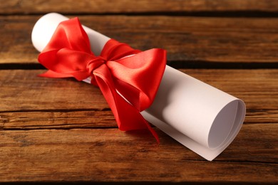 Rolled student's diploma with red ribbon on wooden table