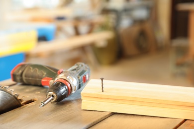 Photo of Carpenter's working place with electric screwdriver and timber strip on table indoors