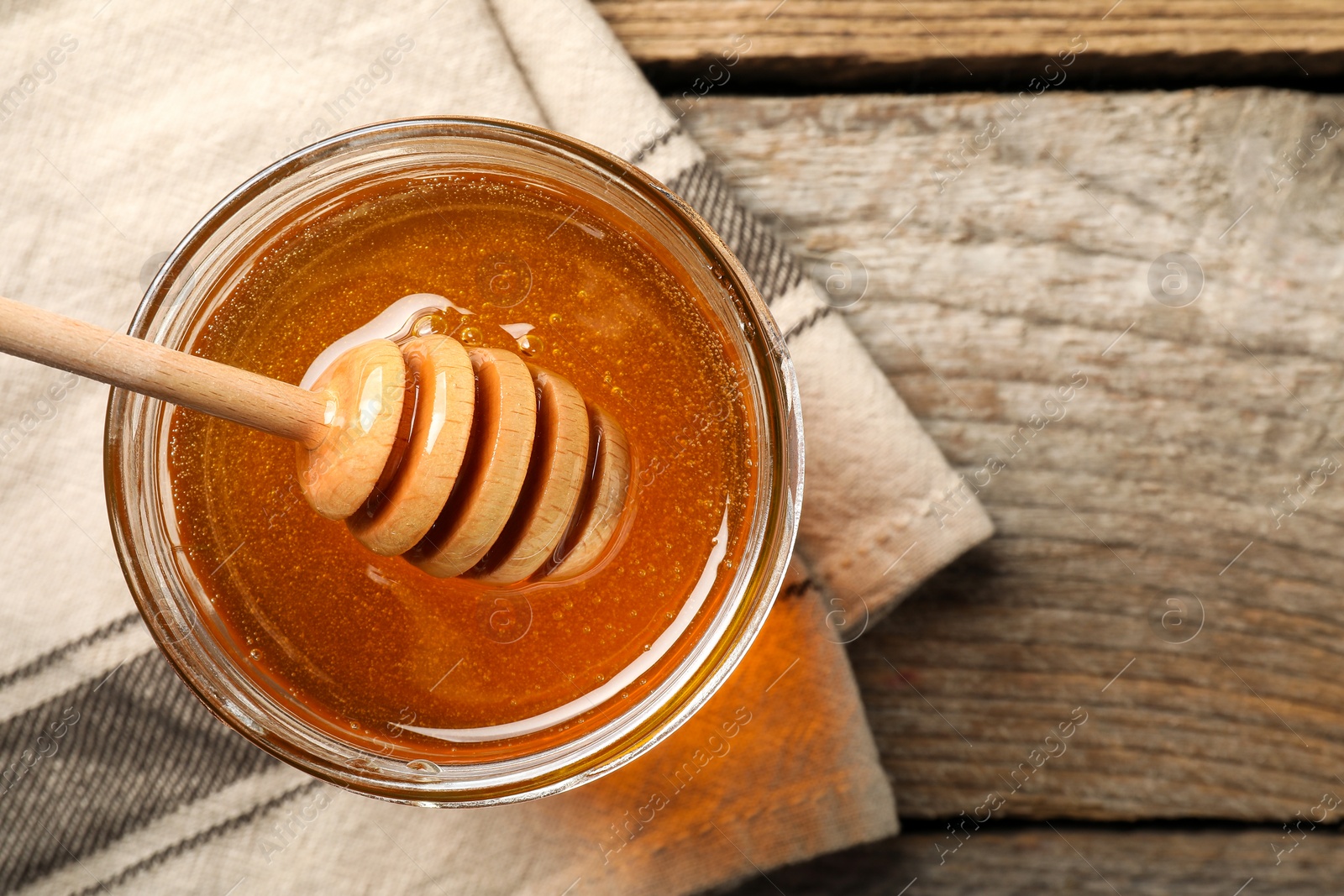 Photo of Dipper with honey in jar on wooden table, top view. Space for text