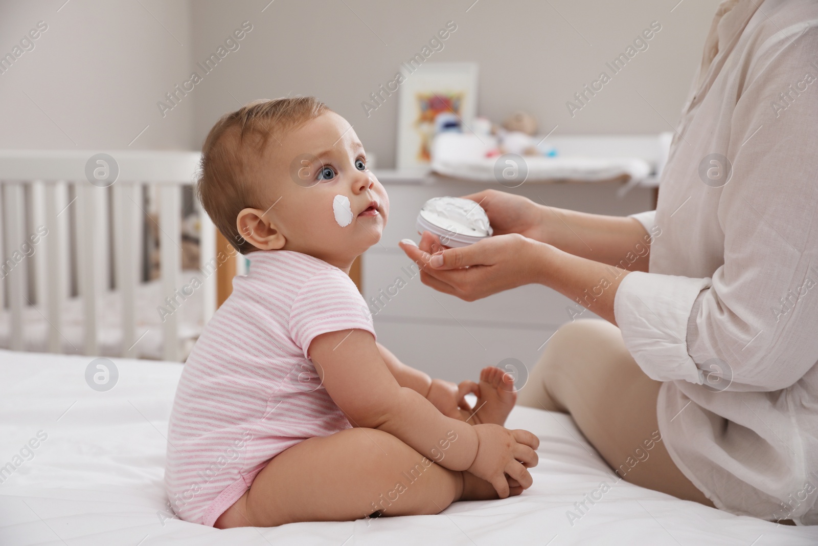 Photo of Mother applying moisturizing cream on her little baby at home, closeup