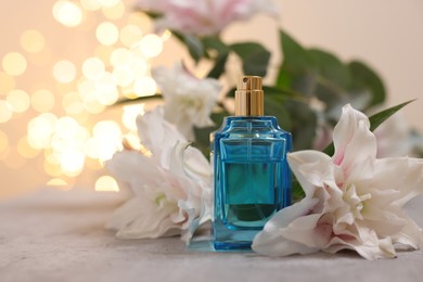 Photo of Bottle of perfume and beautiful lily flowers on table against beige background with blurred lights, closeup