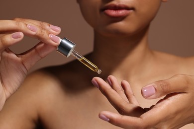 Woman applying serum onto her finger on brown background, closeup