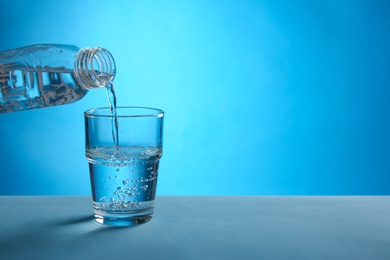 Photo of Pouring water from bottle into glass on blue background. Space for text