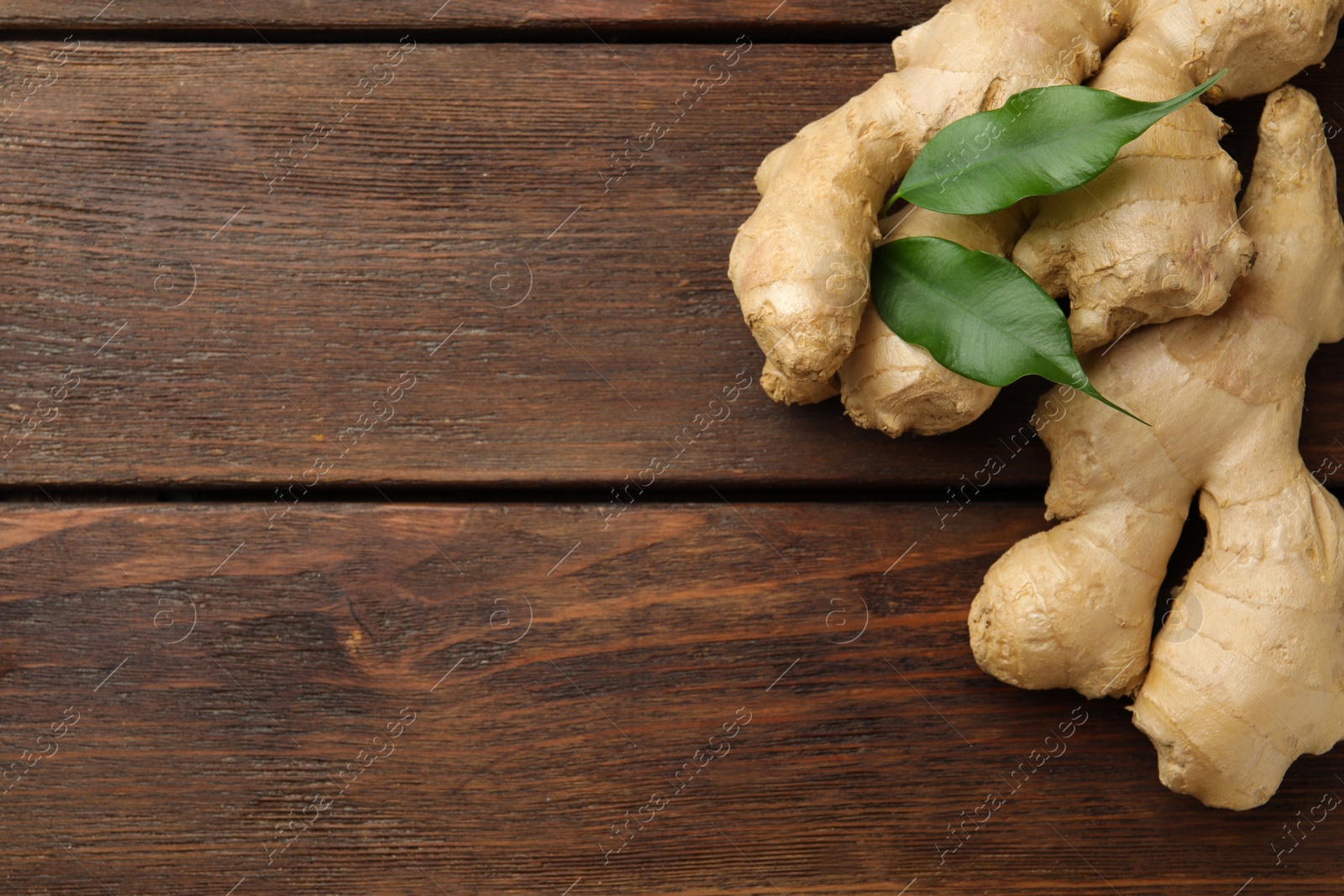 Photo of Fresh ginger with leaves on wooden table, top view. Space for text