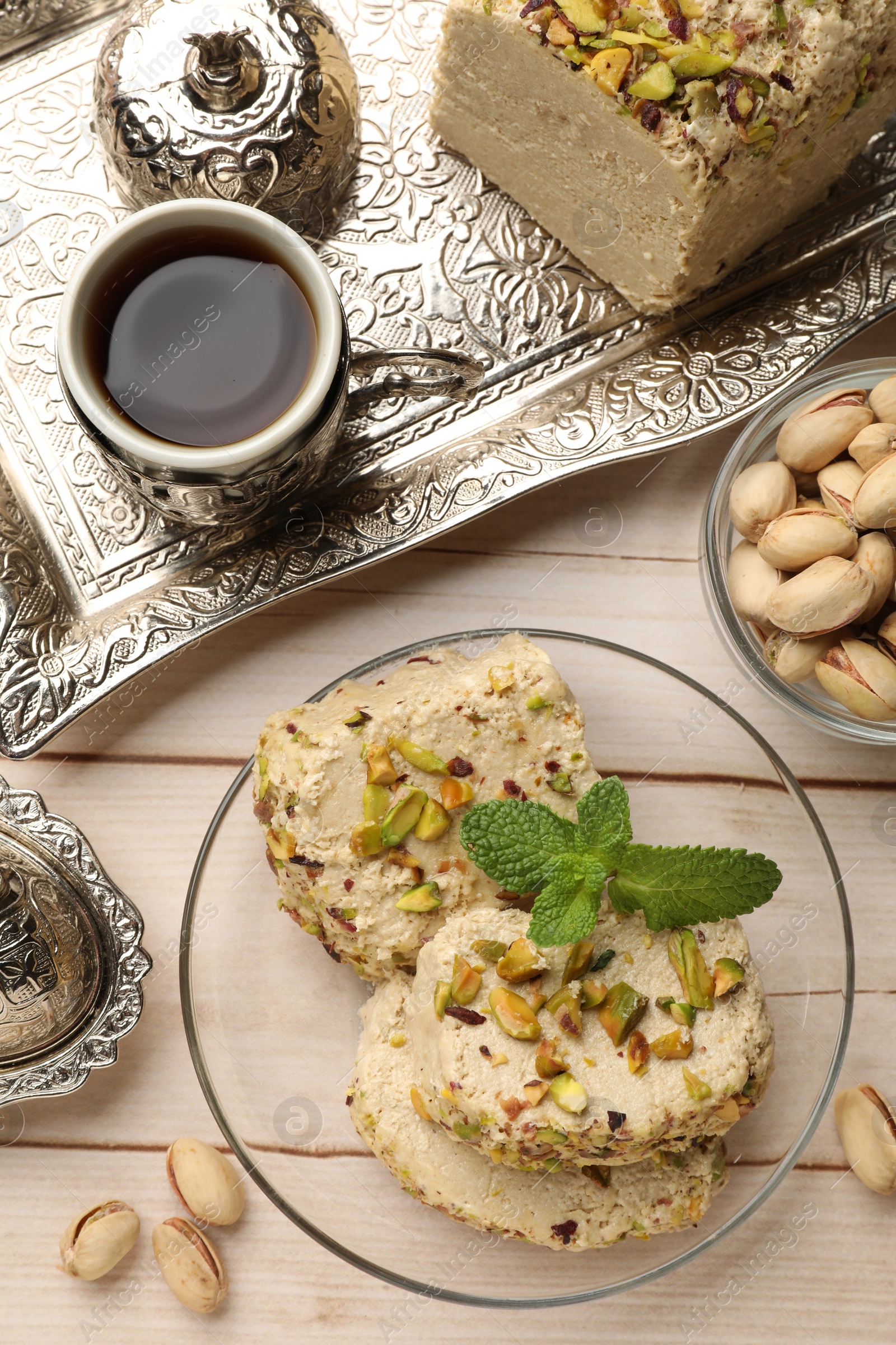 Photo of Tasty halva with pistachios and mint served on wooden table, flat lay