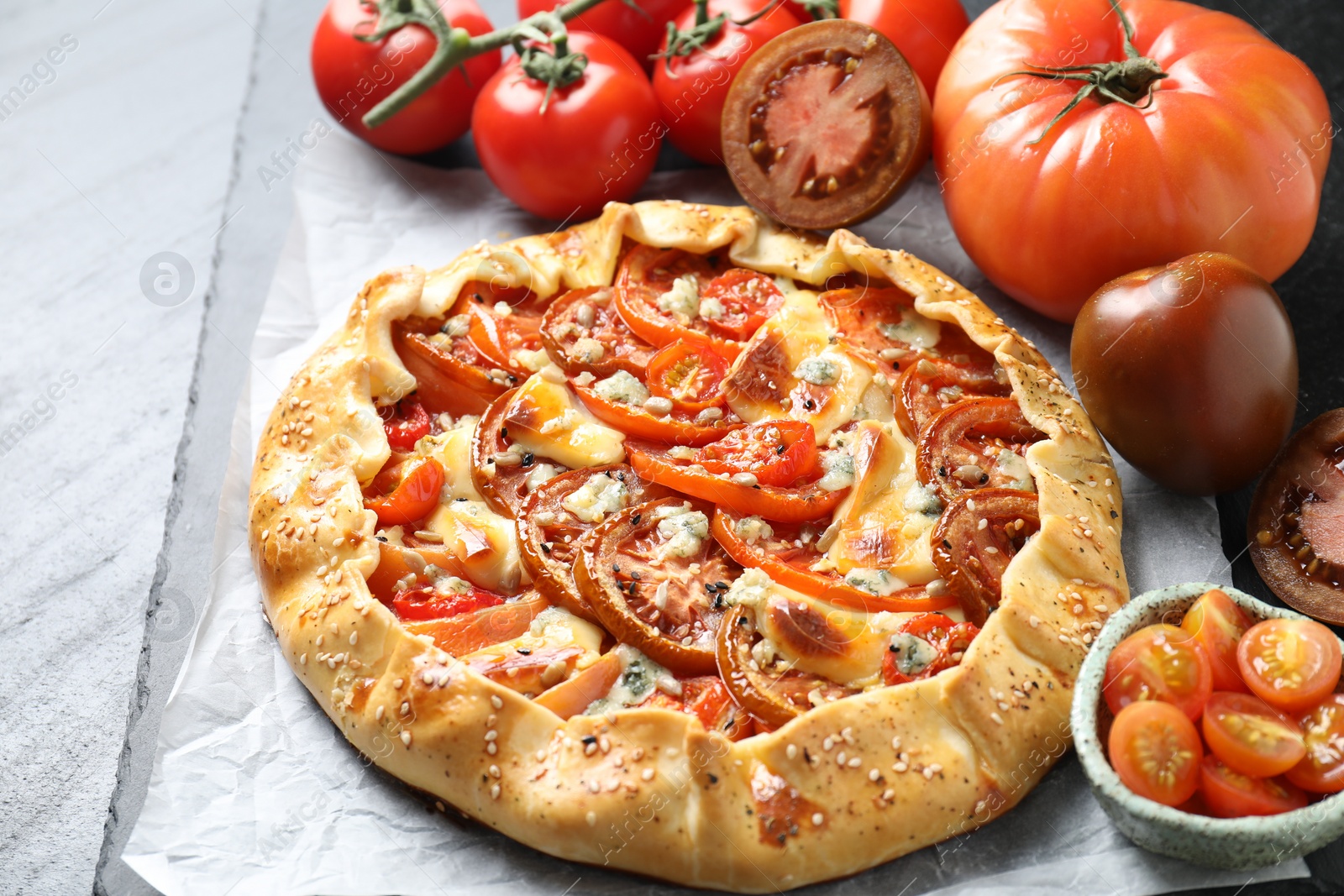 Photo of Tasty galette with tomato and cheese (Caprese galette) on dark textured table, closeup