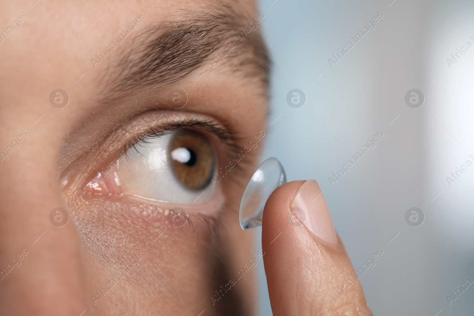 Photo of Man putting contact lens in his eye on blurred background, closeup