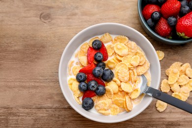 Photo of Bowl of tasty crispy corn flakes with milk and berries on wooden table, flat lay. Space for text
