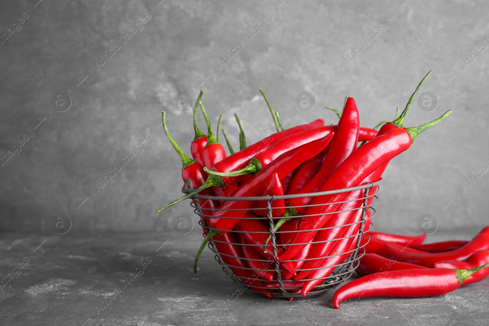 Photo of Basket with ripe chili peppers on grey background