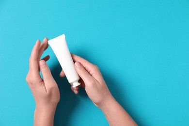 Photo of Woman with tube of hand cream on light blue background, top view. Space for text