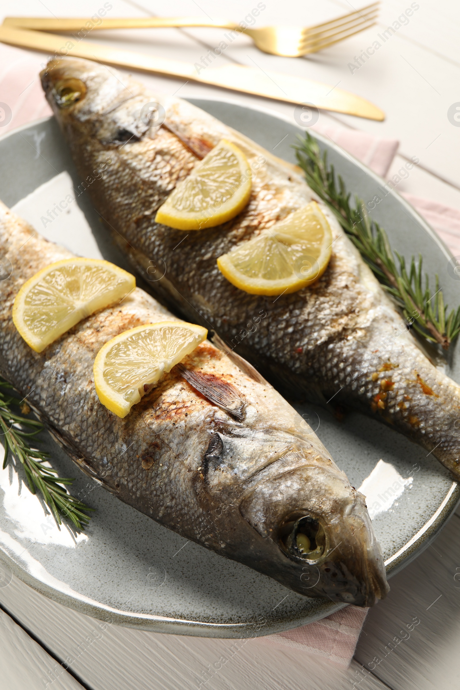 Photo of Delicious baked fish, lemon and rosemary on white wooden table