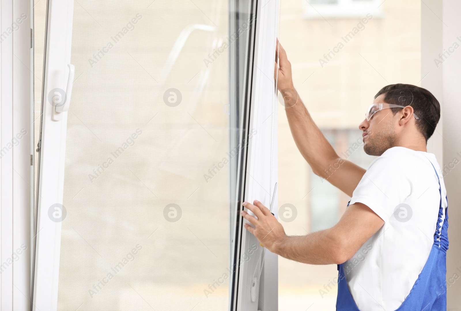 Photo of Construction worker repairing plastic window with screwdriver indoors